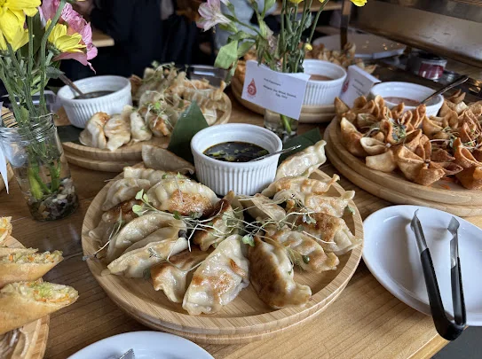 Wooden catering platters of pan-fried dumplings topped with microgreens and crispy folded wontons, served with small bowls of dipping sauce, from Aloy Thai Cuisine in Boulder